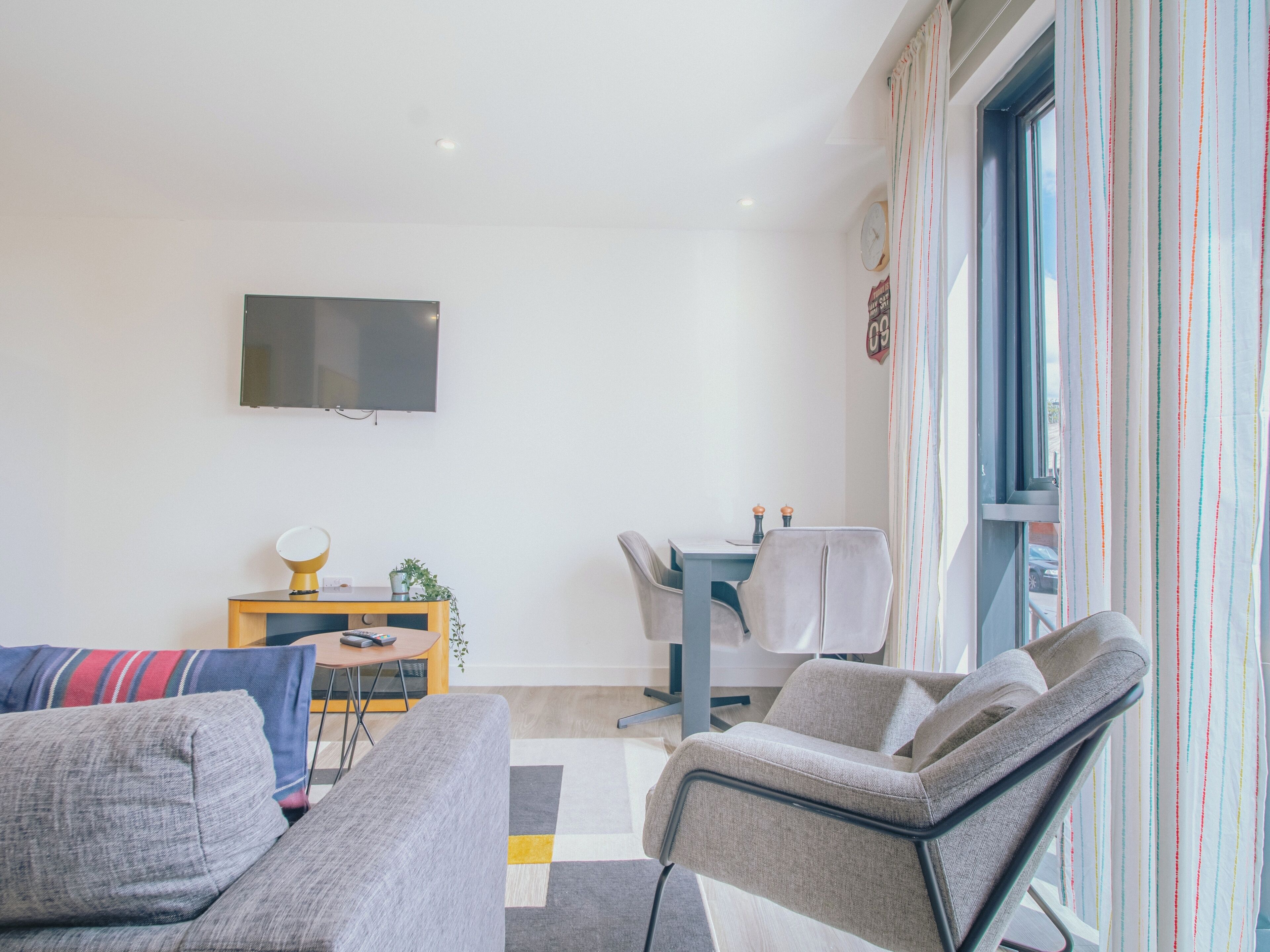 A modern living room with a sofa, armchairs, a small table, and a TV mounted on the wall.