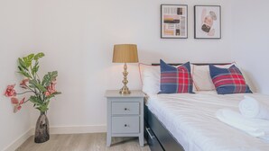 Une chambre bien rangée, avec un lit, une table de chevet, une lampe et un vase rempli de fleurs.