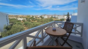 A balcony with a wooden chair and a small round table, overlooking a town with buildings and greenery. - Aristotle Suites, Avgi (Adamantas)