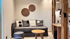A modern living room with a grey sofa, decorative pillows, a round wooden table, and a woven ottoman. - Aristotle Suites, Avgi (Adamantas)