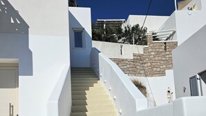 A white staircase leading to a door, surrounded by white walls and a stone wall. - Aristotle Suites, Avgi (Adamantas)