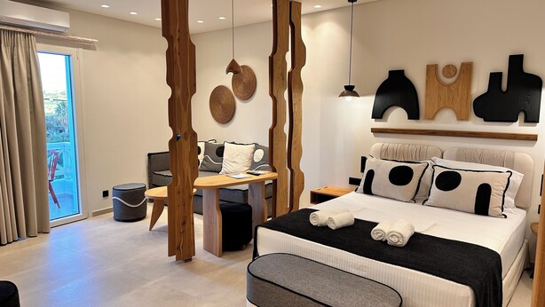 A modern bedroom with a bed, bedside tables, a desk, and a view through a sliding door. - Aristotle Suites, Avgi (Adamantas)