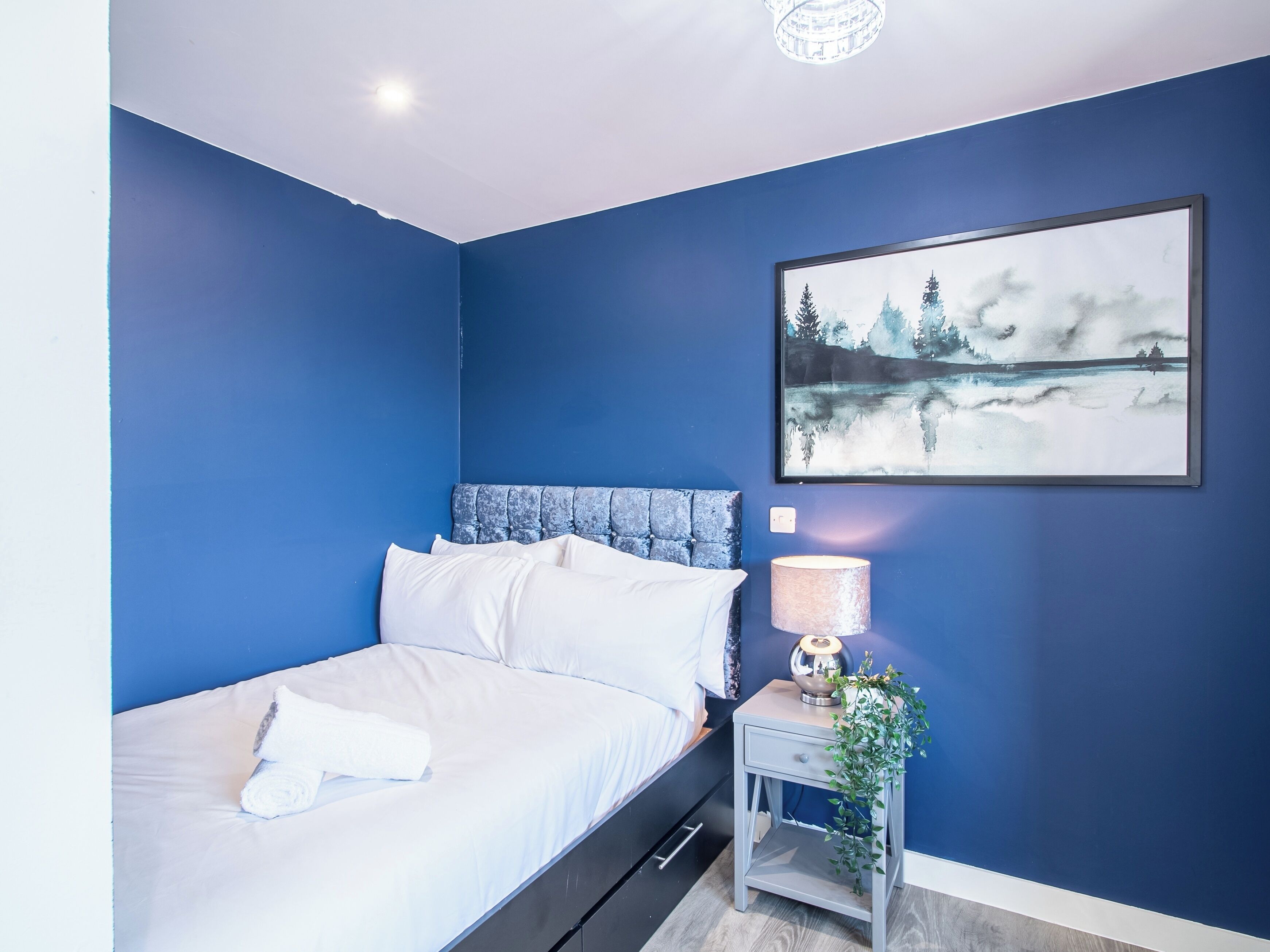 A bedroom with a bed, a nightstand with a lamp, and a painting on the wall.