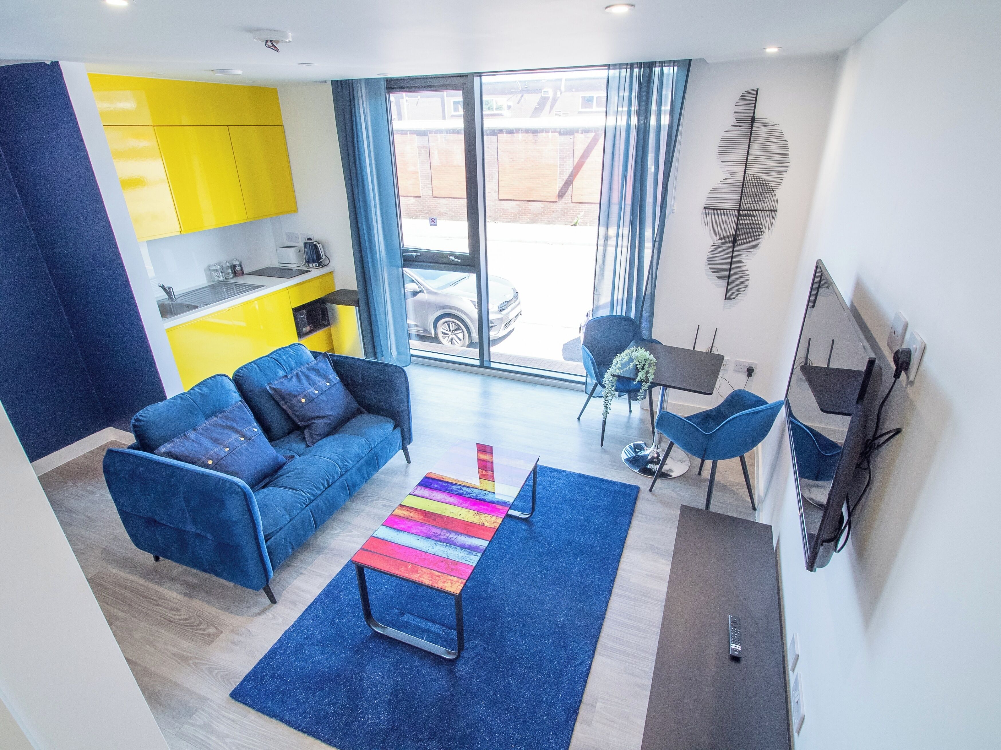 A modern living room with a blue sofa, a colorful striped coffee table, and a TV.