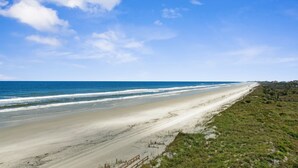 Een strand met een lange zandvlakte, een heldere blauwe lucht en een rustige zee.
