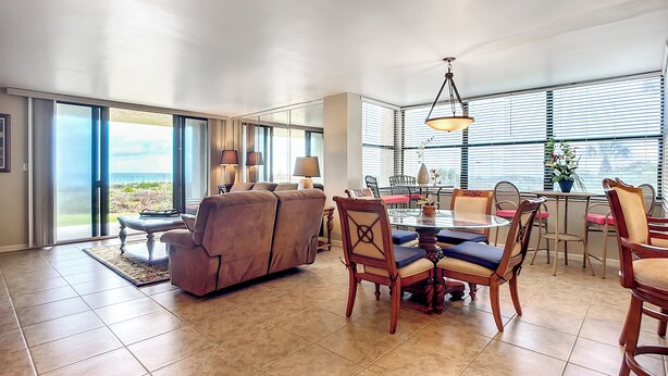 Een ruime woonkamer met een grote schuifpui naar een balkon, een eettafel met stoelen, en een bank.