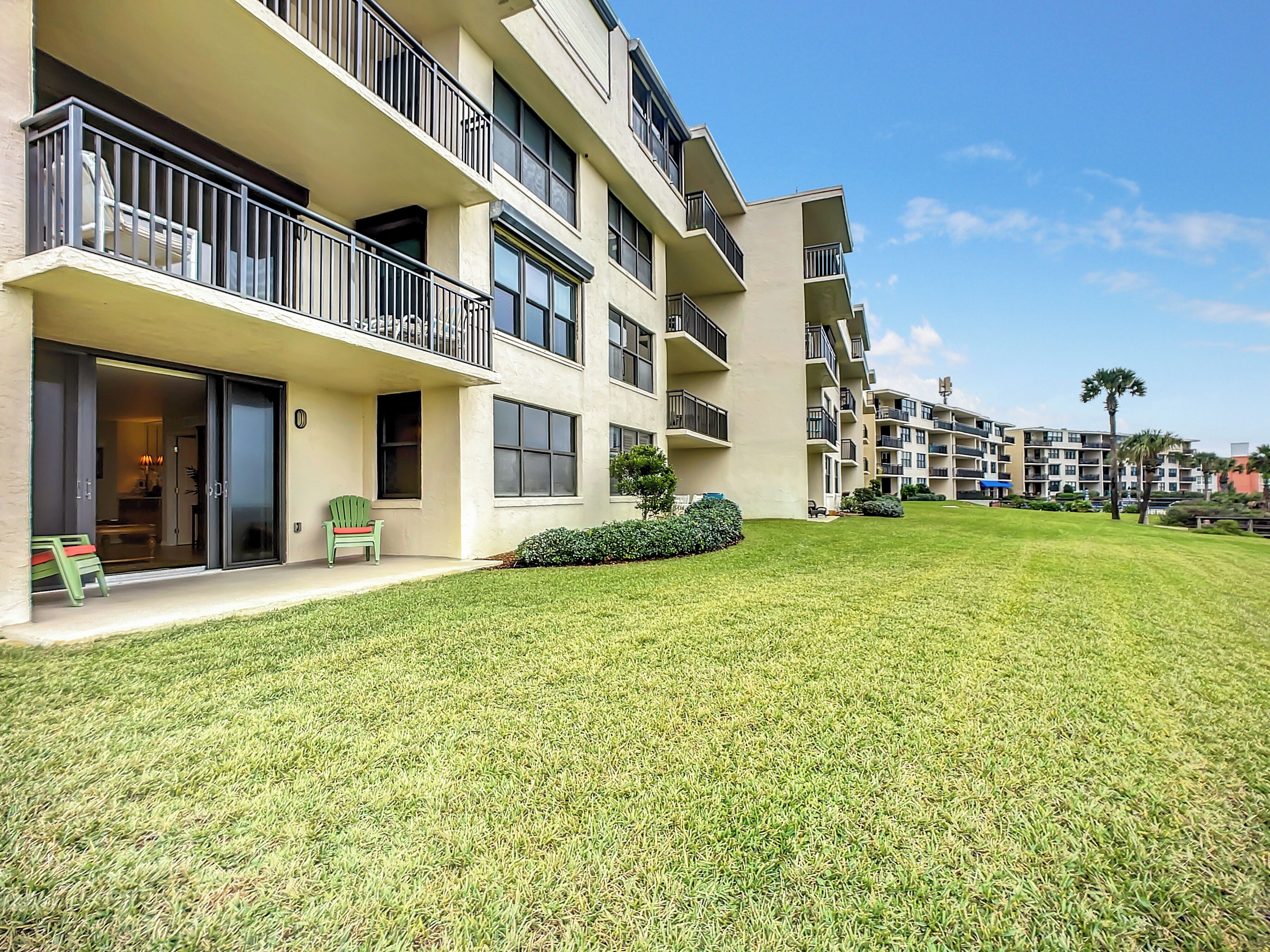 A multi-story residential building with balconies, a well-maintained lawn, and a clear sky.