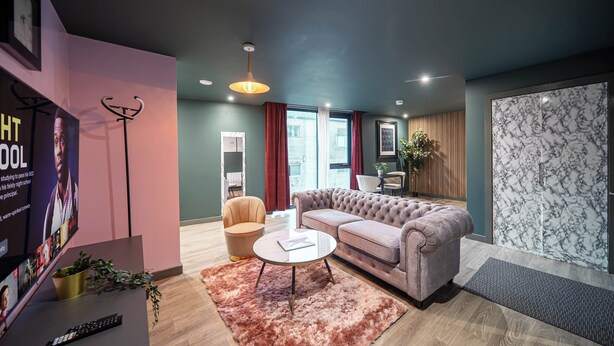 Een moderne woonkamer met een bank, een salontafel en een televisie. Er staat een plant op de vloer en een poster aan de muur.