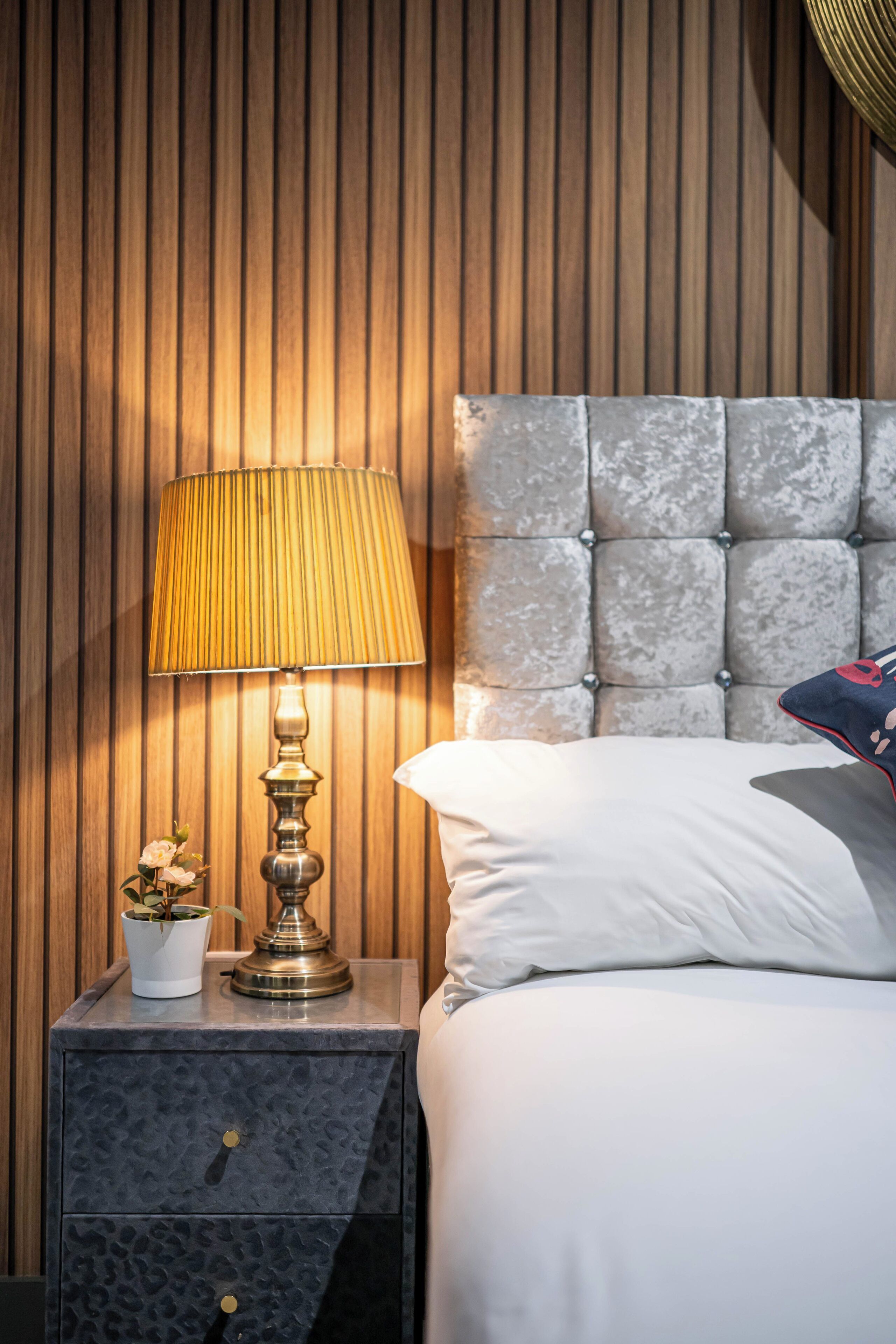 A neatly made bed with a tufted headboard, a bedside lamp, and a small potted plant on a nightstand.