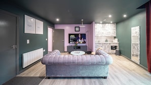 Een moderne woonkamer met een grijze bank, een flatscreen-tv, een klein rond tafeltje en een marmeren spatwand in de keuken.