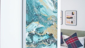 A bedroom with a large abstract painting on the wall, a bed with plaid pillows, and a framed picture on the wall.