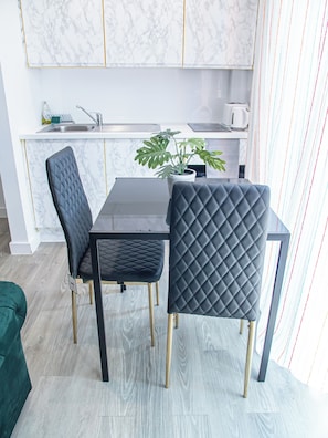 Una cocina moderna con armarios de mármol, un comedor con mesa negra y dos sillas negras con patas doradas.