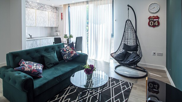 A modern living room with a green sofa, a hanging chair, and a glass coffee table.