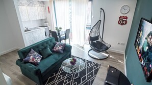 A modern living room with a green sofa, a hanging chair, a glass coffee table, and a TV displaying a movie.