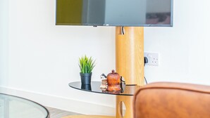 Un téléviseur à écran plat fixé sur un support en bois, une petite plante en pot et un objet décoratif posé sur une table en verre.