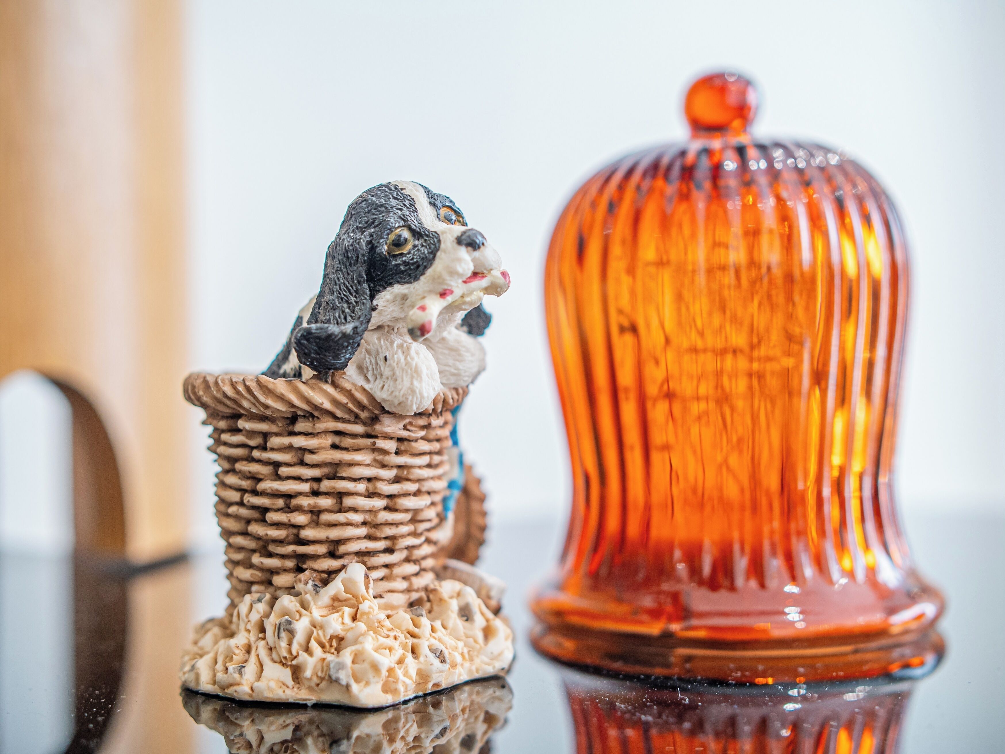 Una cesta de mimbre con una figurita de un perro y un perro pequeño, junto a una campana de cristal.