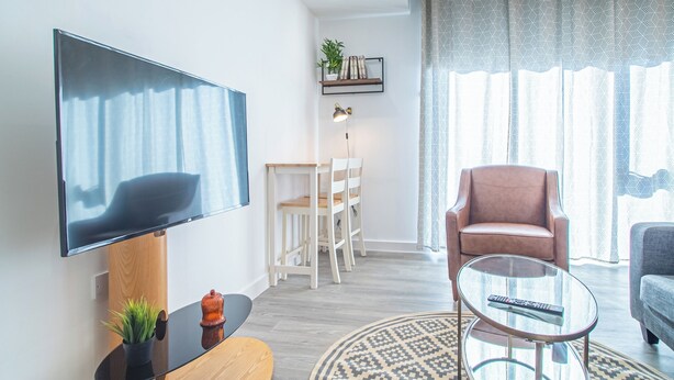 Un salon moderne doté d’un téléviseur à écran plat, d’une table basse ronde en verre, d’un fauteuil rembourré et d’un canapé.