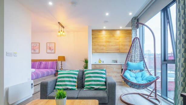 A modern living room with a grey sofa, a hanging chair, a coffee table, and a kitchen in the background. - Priestley Street Apartment in Sheffield (Sheffield)