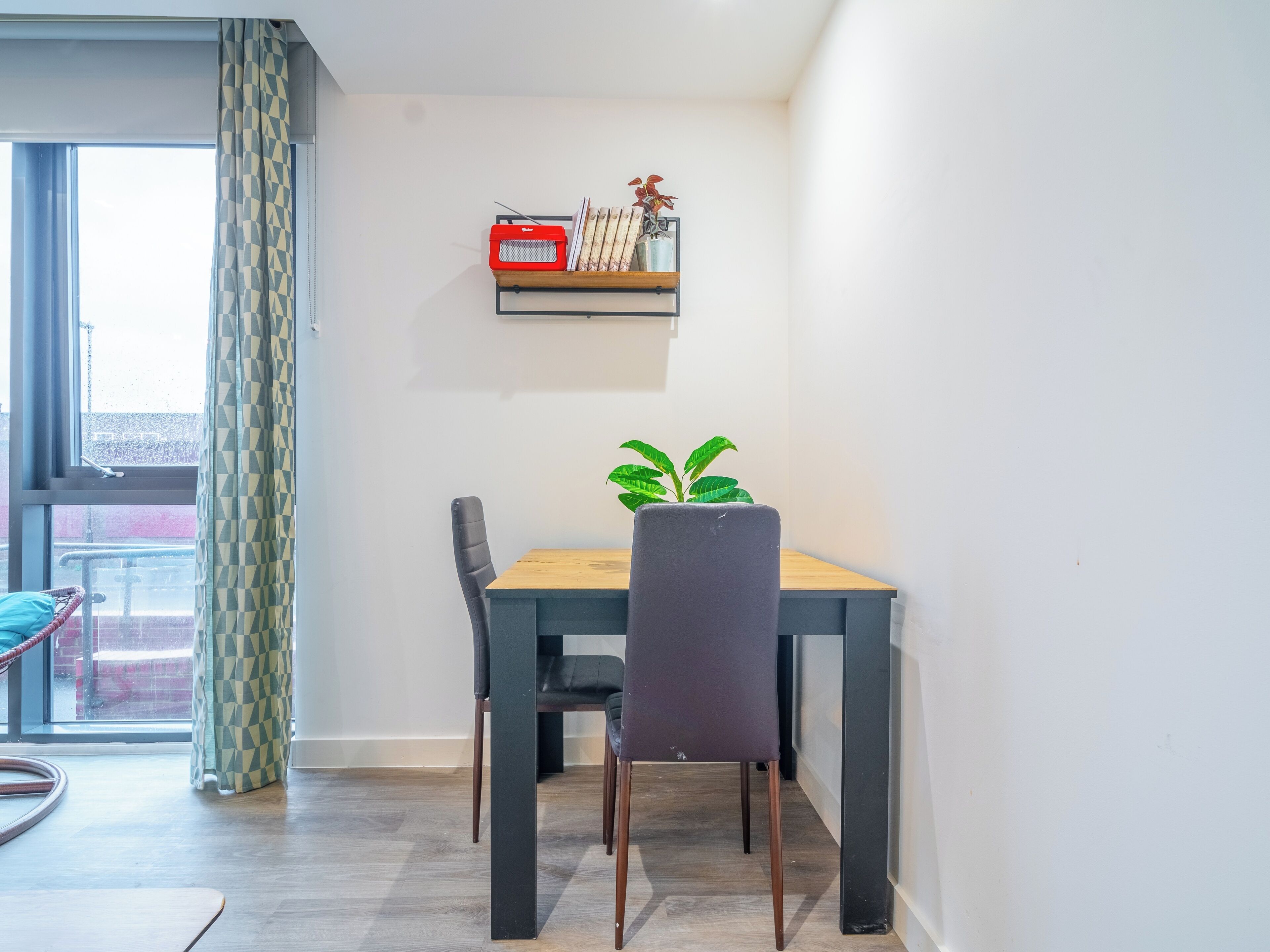 Un comedor con una mesa, sillas, una planta en maceta y una estantería con objetos decorativos.