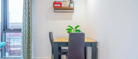 Un comedor con una mesa, sillas, una planta en maceta y una estantería con objetos decorativos.