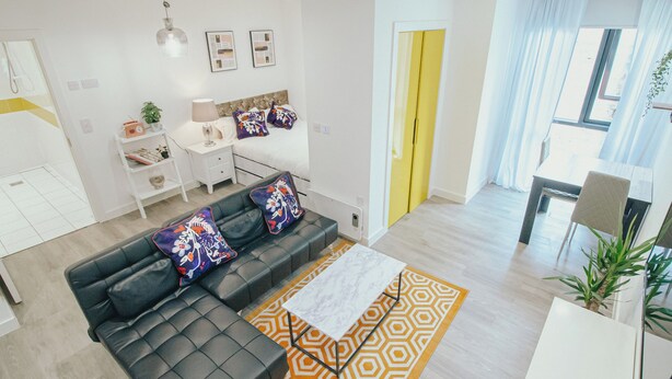 A modern living room with a black leather sofa, a patterned rug, and a dining area with a table and chairs. - Lovely Triple Studio in Sheffield City Centre (Sheffield)