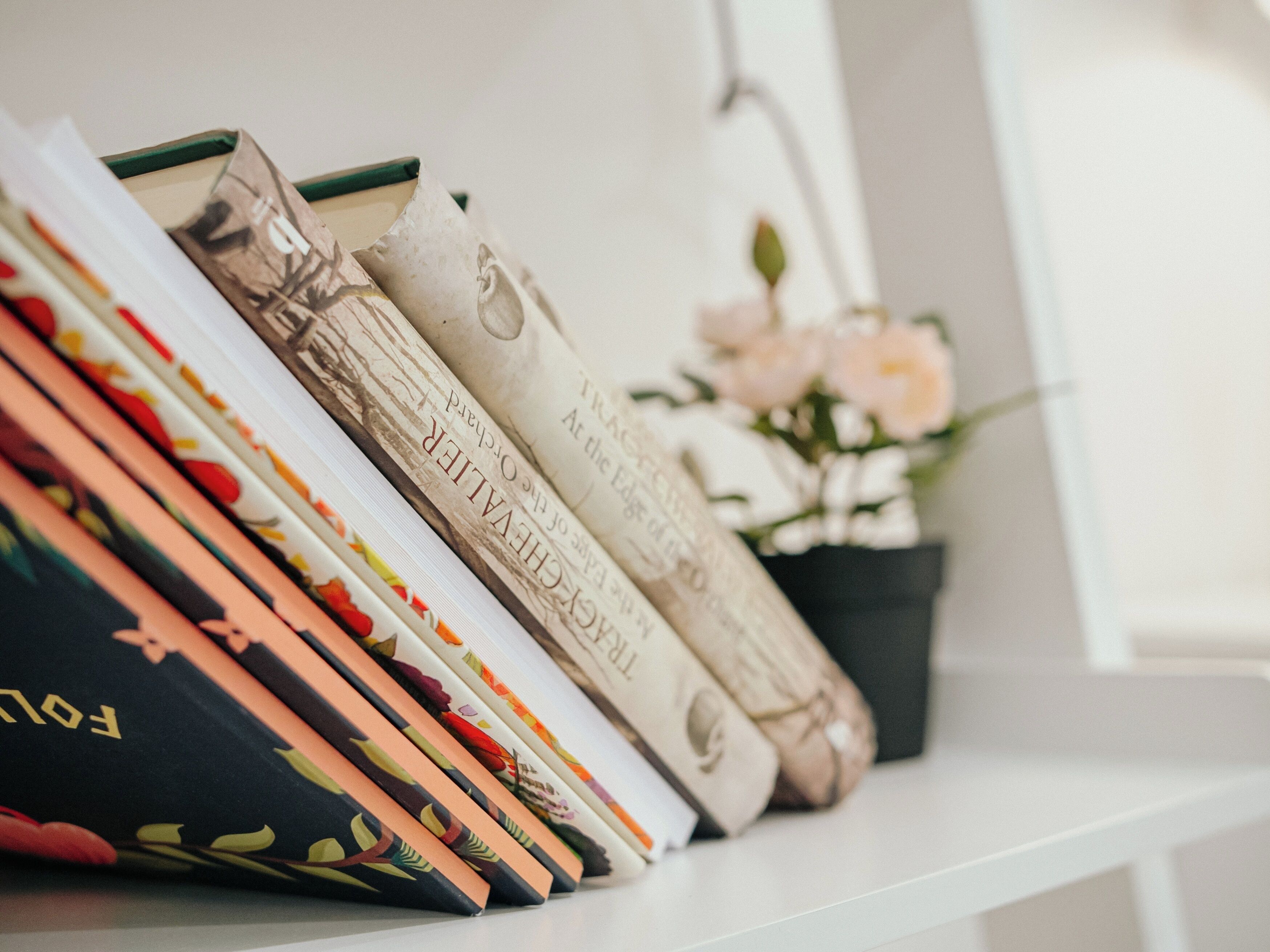 Une rangée de livres aux motifs floraux, disposés sur une étagère blanche.