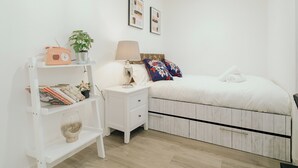 A bedroom with a bed, nightstand, lamp, shelf with books, and a radio. - Lovely Triple Studio in Sheffield City Centre (Sheffield)
