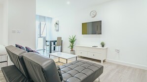 A modern living room with a sofa, a coffee table, a TV mounted on the wall, and a dining area with chairs and a table. - Lovely Triple Studio in Sheffield City Centre (Sheffield)