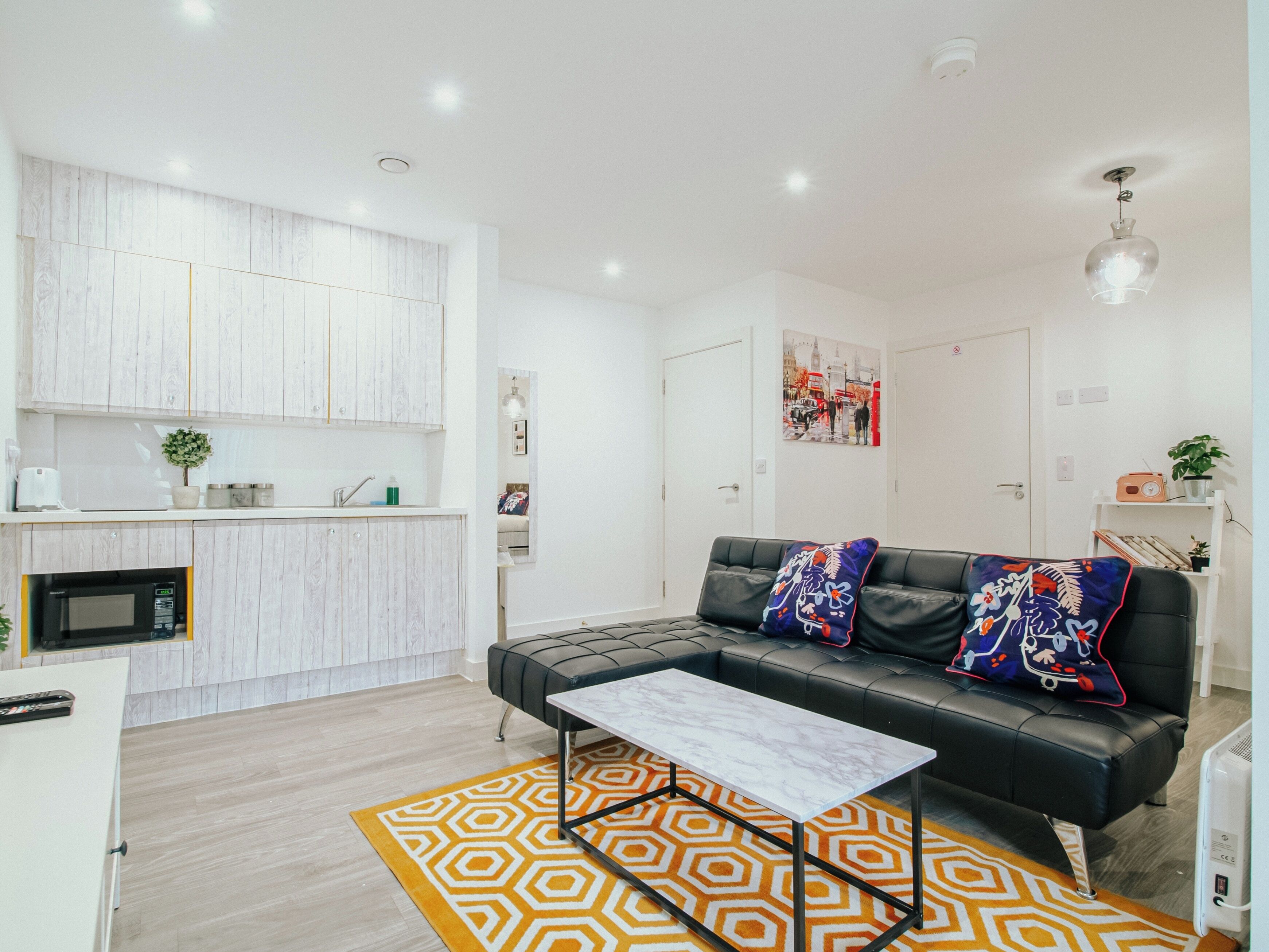A modern living room with a black leather sofa, a white coffee table, and a patterned rug.