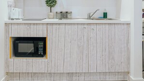 A kitchen with wooden cabinets, a microwave, a sink, and a small potted plant. - Lovely Triple Studio in Sheffield City Centre (Sheffield)