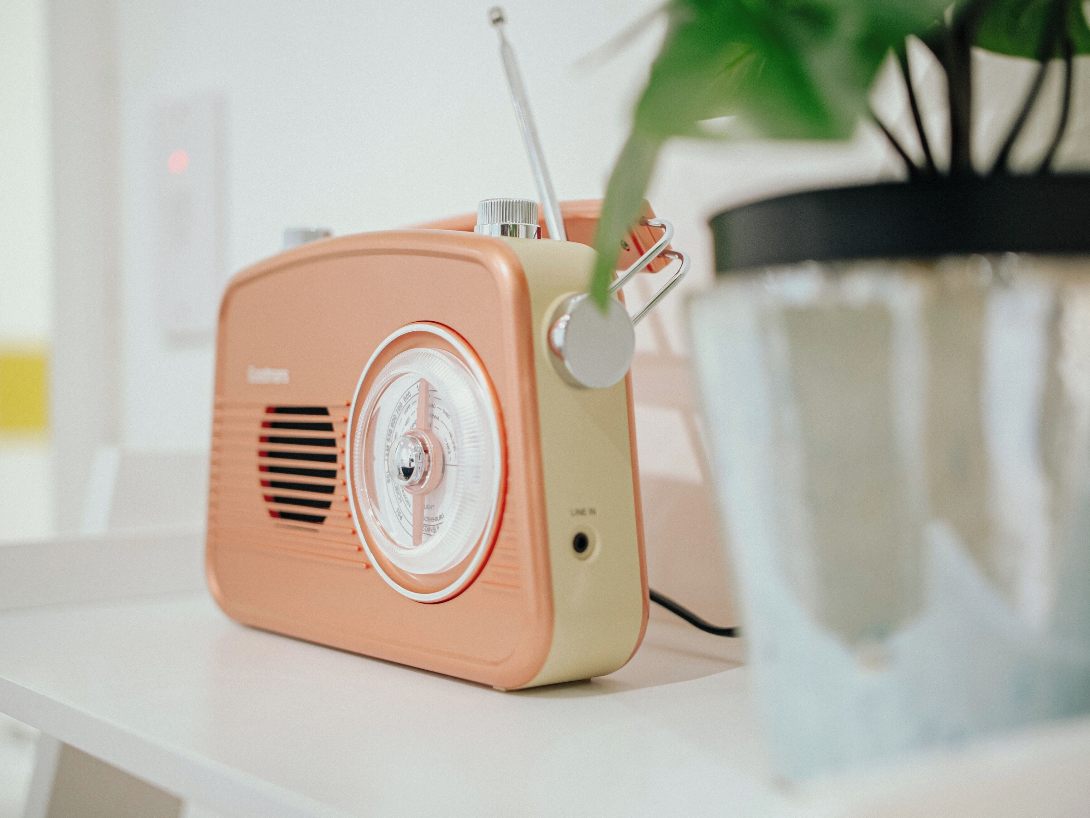A retro-styled radio with a clear dial, placed on a white surface next to a potted plant.