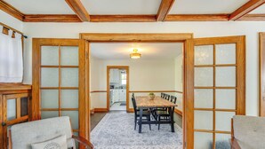 Un coin repas avec une table et des chaises en bois, un tapis à motifs et une vue sur la cuisine par une porte ouverte.
