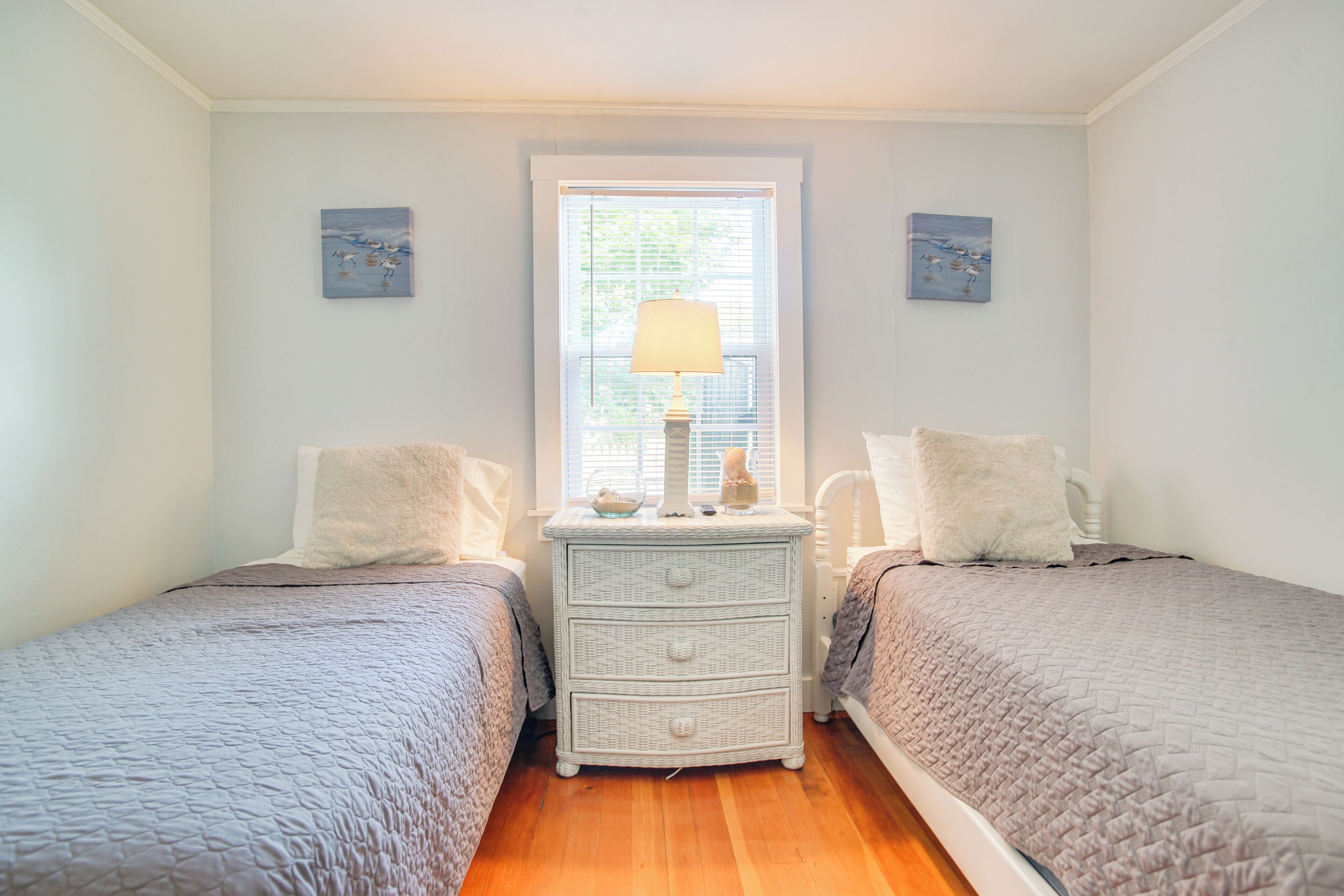 Un dormitorio con dos camas, una mesita de noche, una ventana con lámpara y decoración en la pared.