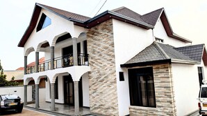 A two-story house with a balcony, a stone facade, and a car parked in front. - Kigali Nice Apartment  (Kigali)