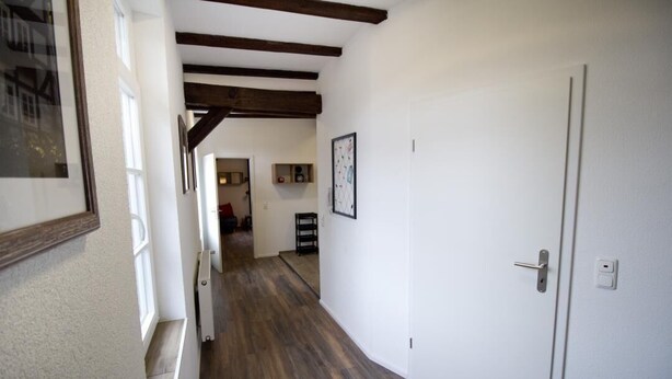A hallway with wooden floors, white walls, and exposed beams. There is a door on the right and a framed picture on the left. - NEW! Apartment Märchenstube (Alsfeld)