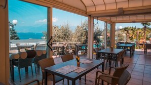 An outdoor dining area with tables and chairs, large windows offering a view of the sea and trees. - Internazionale Eden Mobilehome Happy Relax for 6 people (San Felice del Benaco)