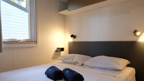 A neatly made bed with white linens and two towels, a bedside lamp, and a window with blinds. - Internazionale Eden Mobilehome Happy Relax for 6 people (San Felice del Benaco)