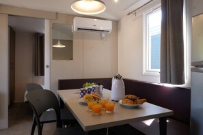 A dining area with a table set for breakfast, including croissants and juice, and a window with curtains. - Internazionale Eden Mobilehome Happy Relax for 6 people (San Felice del Benaco)