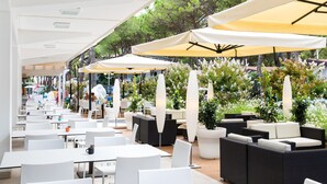 An outdoor cafe with white tables and chairs, yellow umbrellas, and potted plants. - Vacation park Residence Village Mobilehome Happy Relax for 6 persons (Cavallino Treporti)