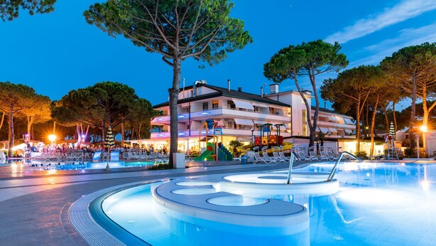 A swimming pool with a modern design, surrounded by lounge chairs and a building with multiple balconies. - Vacation park Residence Village Mobilehome Happy Relax for 6 persons (Cavallino Treporti)