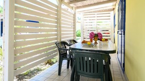 Un espace extérieur abrité, aménagé pour prendre les repas, avec une table et des chaises, un pot de fleurs et une vue sur la rue.