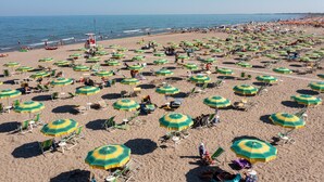 Une plage avec de nombreux parasols et des chaises longues aux rayures vertes et jaunes.