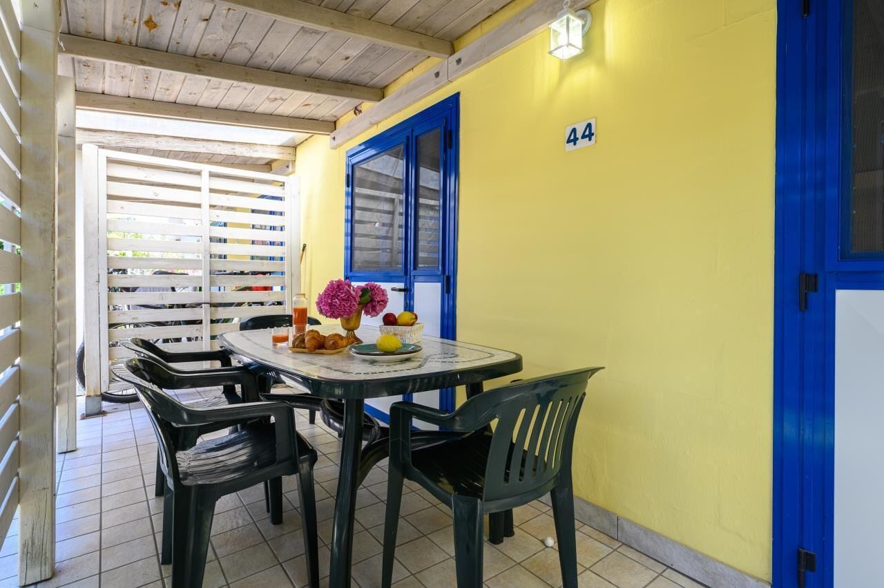 A dining area with a round table, chairs, and a small table with fruits and flowers.