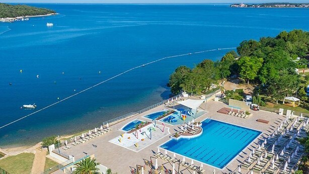 Un resort con una grande piscina, sdraio e vista sul mare.