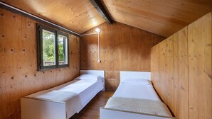 Ein Zimmer mit zwei Einzelbetten, Holzwänden, einem Fenster und einer Nachttischlampe.