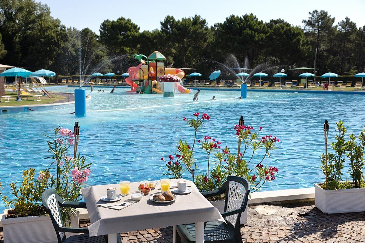 A pool area with a table set for breakfast, surrounded by flowers and umbrellas.