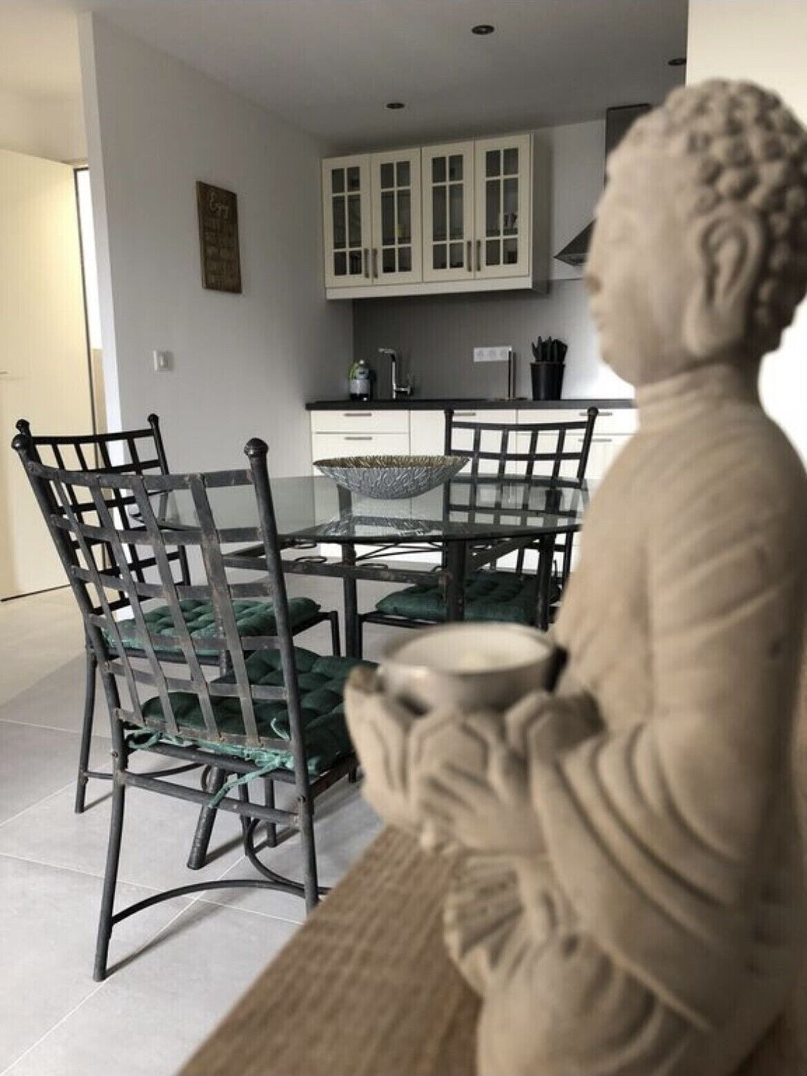 Un espace repas avec une table et des chaises, une statue et, au fond, une cuisine.