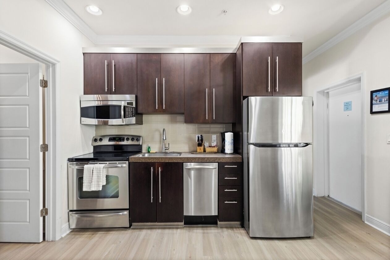 A modern kitchen with dark wooden cabinets, stainless steel appliances, and a light wood floor.