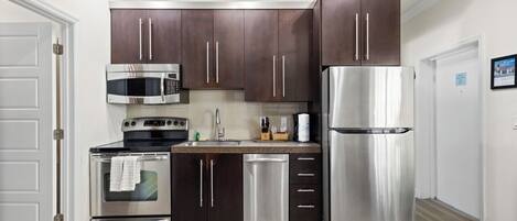 A modern kitchen with dark wooden cabinets, stainless steel appliances, and a light wood floor.