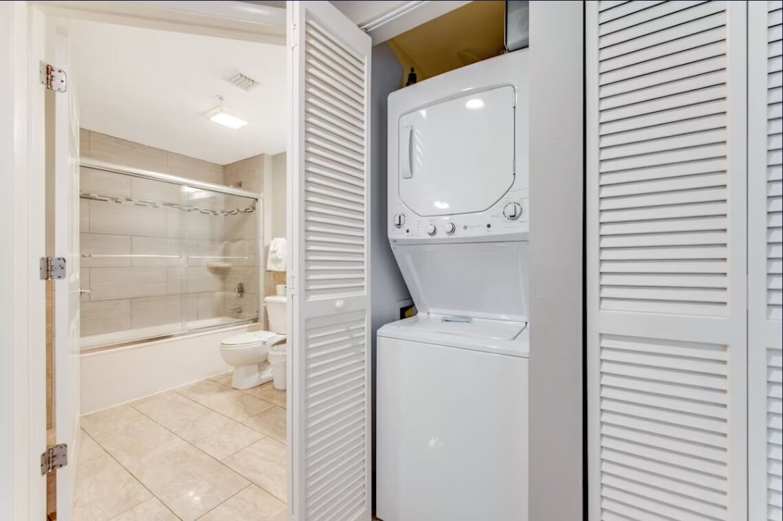 Un baño con cabina de ducha de vidrio, inodoro y lavadora incorporada.